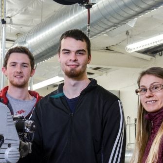 Three students by engine in lab. 