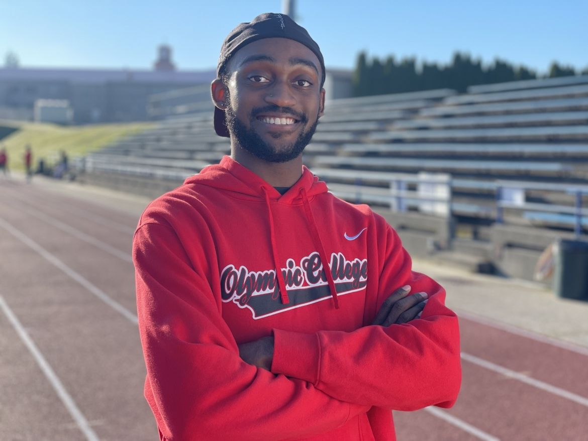 Student smiling and wearing Olympic College sweatshirt, with arms crossed, on the Bremerton High School Track