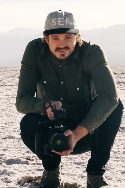 Marq Evans crouching on a beach and holding a video camera