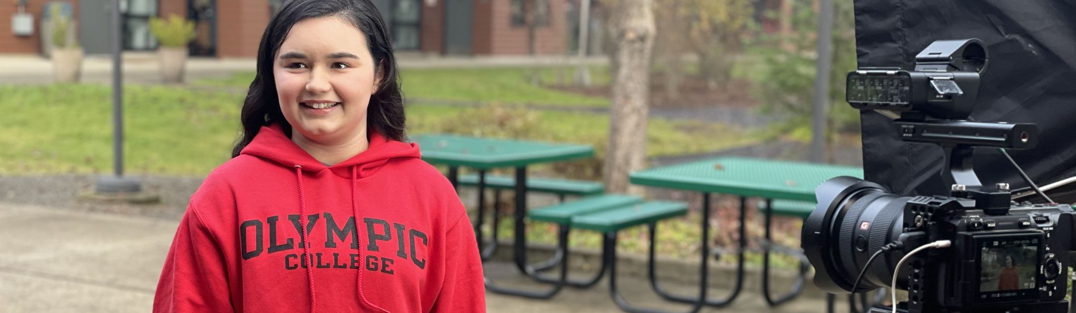 Student on Shelton campus in red sweatshirt and smiling for the camera.