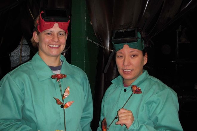 Two women in welding goggles holding their rose project
