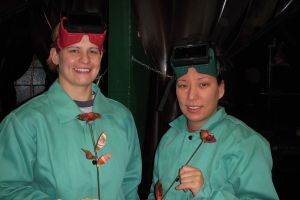 Two women in welding goggles holding their rose project