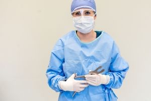 Surgical Technology student wearing surgical scrubs, gloves, and mask while holding surgical equipment