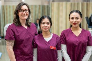 Three sonography students wearing red scrubs smiling at the camera