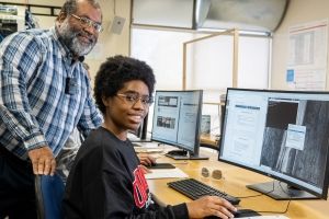 Student and instructor smiling at camera as they work at a computer station
