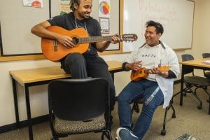 Two students in a classroom, one playing the guitar, the other playing a ukulele