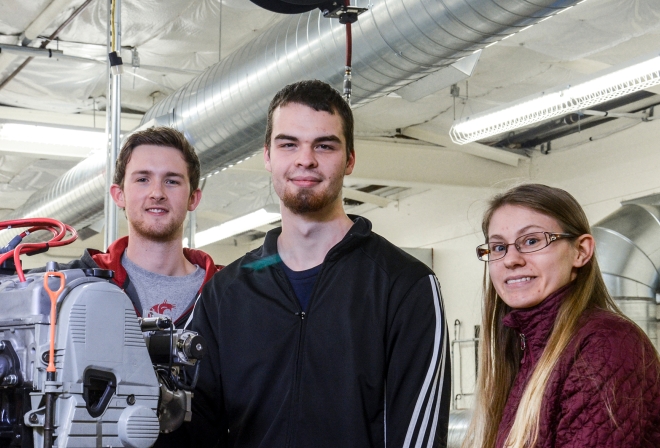 Three students by engine in lab.