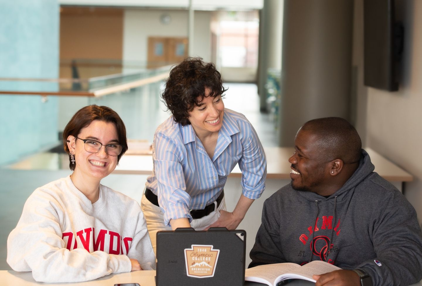 A faculty member with two students on either side of them, all looking at a tablet computer on the table in front of them.