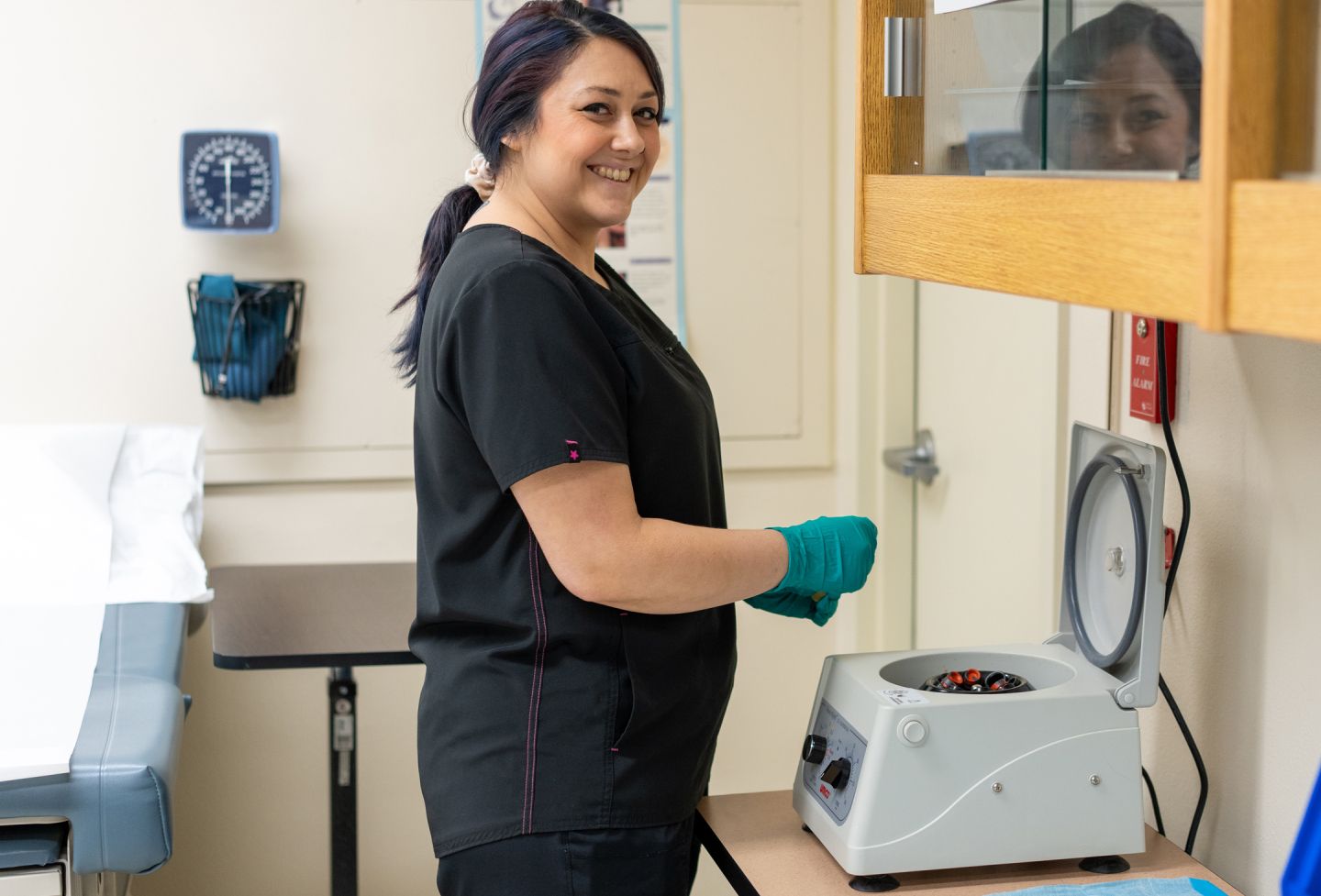 Smiling phlebotomy student in black scrubs standing in front of a centrifuge