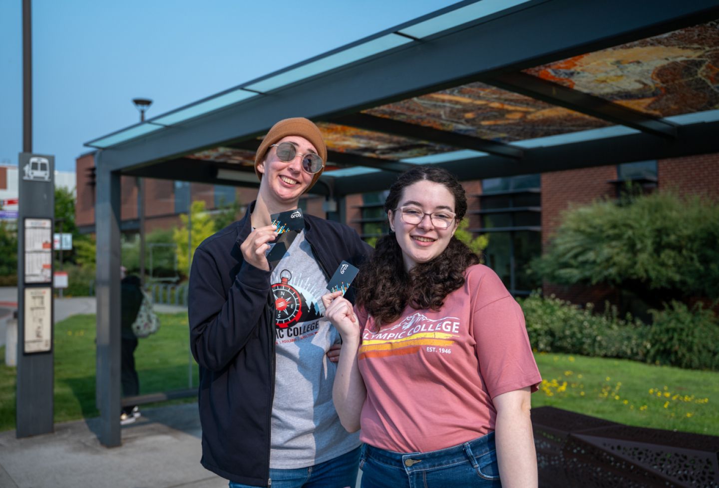 Two students in front of bus stop holding bus passes