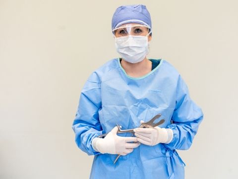 Surgical Technology student wearing surgical scrubs, gloves, and mask while holding surgical equipment