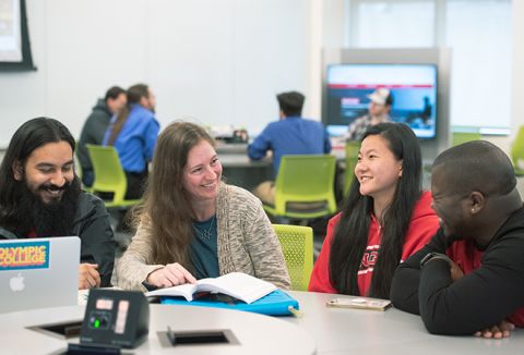 Teacher with students at desk with laptop.