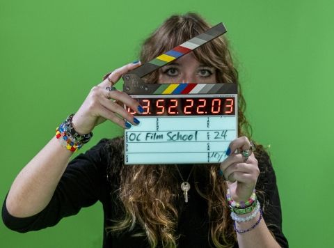 Film student operating clapperboard in front of green screen