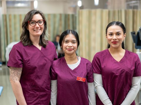 Three sonography students wearing red scrubs smiling at the camera