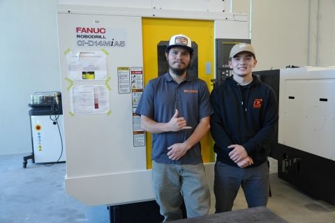 Welding students Justin Adams and Colin DeGross pose in front of a piece of equipment in the newly renovated Shops building