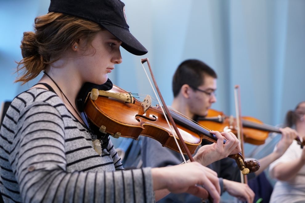 Female student in baseball cap playing the violin in class