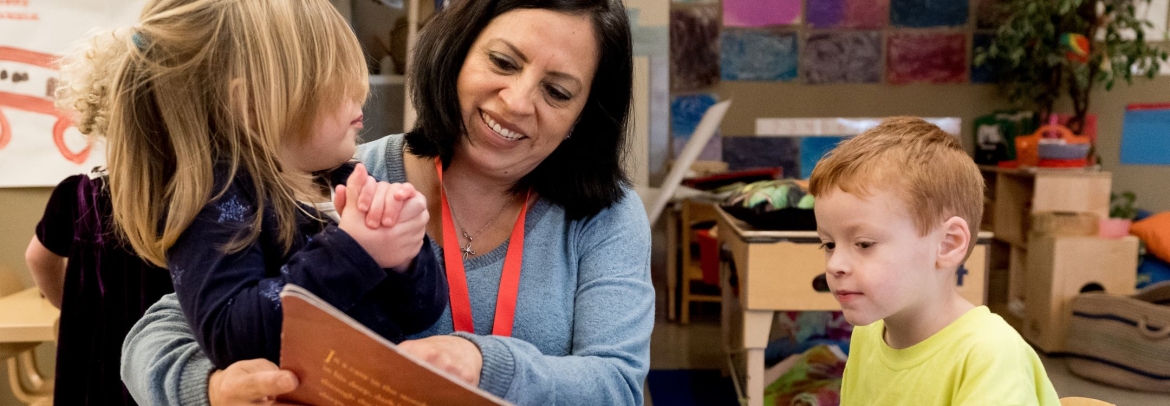 Smiling female teacher sitting closely with kids showing them a book